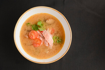 Vegetable soup with salmon in white bowl over black background. Dinner concept, healthy hot soup.