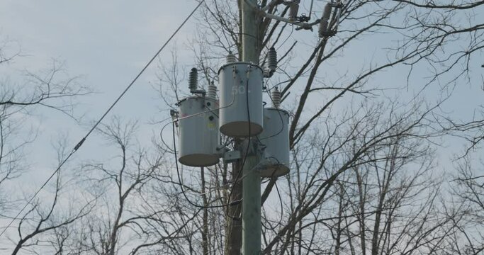 Three Hydro Quebec transformers mounted on a wood hydro pole in the middle of the woods with spring trees and blue sky in the background in Gatineau, Quebec. 