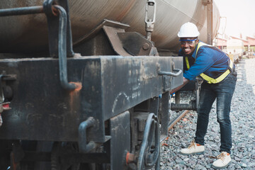 African machine engineer technician wearing a helmet, groves and safety vest is using a wrench to repair the train