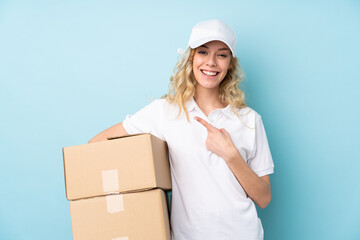 Young delivery woman isolated on blue background pointing finger to the side