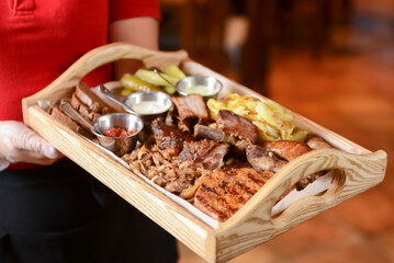 Mixed grilled meat with pepper sauce on a wooden board served by waiter in restaurant or diner.