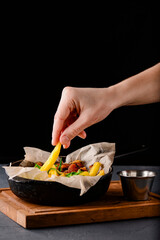 Fried potatoes in an iron pan over rustic wooden board and black background. Rustic style dinner.