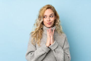 Young blonde woman wearing a sweater isolated on blue background scheming something