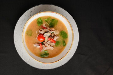Mushroom soup of chicken broth, mushrooms, cherry tomato served in a white bowl over black background.