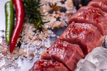 slicing for barbecue of fresh raw fresh meat on crushed ice with rosemary on a background of dark slate stone, top view. sloping horizon. Selective focus. Carnivores concept