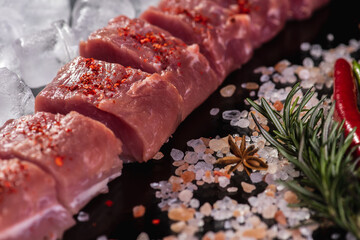 slicing for barbecue of fresh raw fresh meat on crushed ice with rosemary on a background of dark slate stone, top view. sloping horizon. Selective focus. Carnivores concept