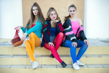 Three pretty girls dressed in the style of the nineties are sitting on the steps.