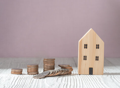 Money coin stack with wooden house model on white wood background. Property investment and house mortgage financial concept. Banking and finance, loan and loss benefit concept.