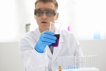 A male chemist holds test tube of glass in his hand overflows a liquid solution