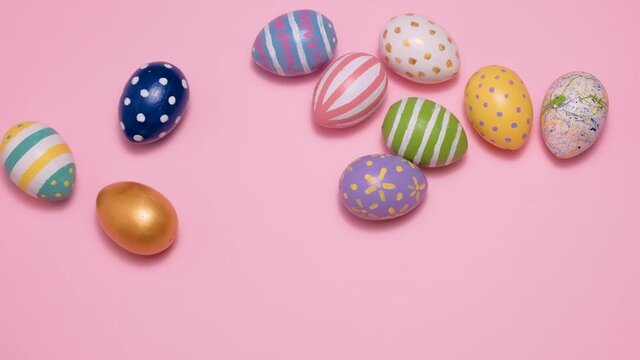 Video of Happy Easter. Colorful painted Easter eggs roll and knock each other on a pink background. Hello spring and easter concept. 4k video.