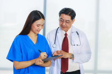 Senior Asian male doctor wearing eye glasses with young female doctor with write board are meeting in a meeting room in the hospital.