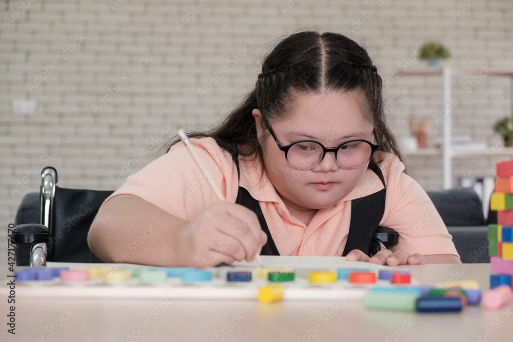 Wall mural young girl with autism on wheelchair is writing and practicing fun playing with toys at home with his mother. Autistic young students are learning with teachers happily.