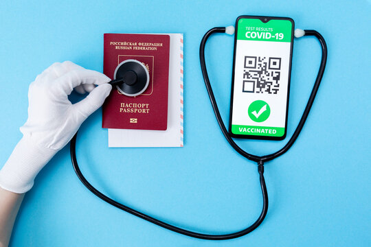 A hand in protective glove control a a passport with help of a stethoscope. Cellphone screen with an electronic health passport with qr-code. Flat lay. Concept of Covid-19 test for travel