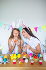 Mother and her little daughter painting eggs. Happy family preparing for Easter.