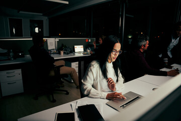 Female employee busy in her work on laptop in office and with colleagues at background