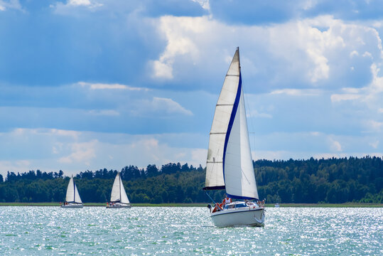 Sailing yacht in the lake with gloomy sky before the rain. Yacht sailing on the lake against a blue sky with clouds. Sailboat vacations on a lake - Powered by Adobe
