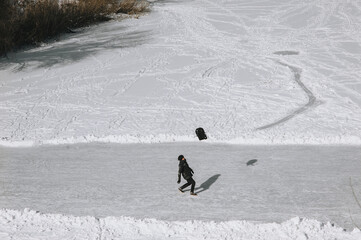 A cheerful man, a tourist throwing a backpack up, slips on slippery ice in black clothes, and falls down while walking along the river in winter. Photography, copy space.