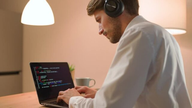 Male programmer is working on creating software, typing program code on a laptop keyboard, programmer at work, a freelancer at remote work at home.