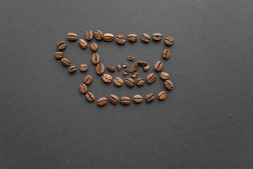 A cup of coffee is lined with roasted beans on a black background top view