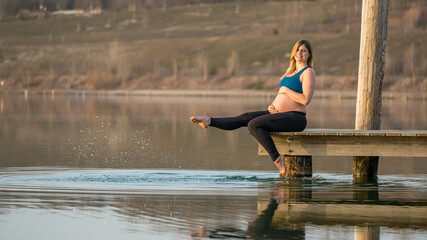 Portrait of a young happy pregnant woman sitting on a jetty at the Störmthaler lake near Leipzig
