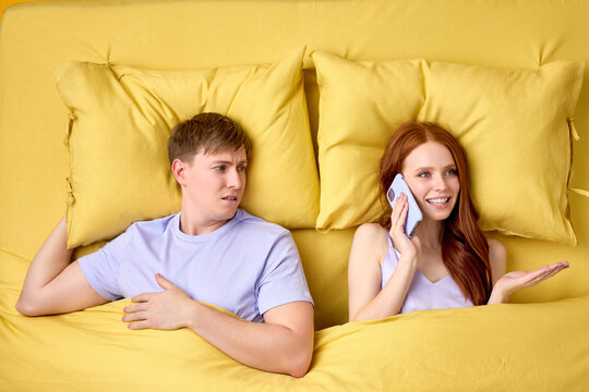 Alienated Millennial Young Couple in Bed, Woman talk on Phome With Someon, Does't Pay Attention On Husband