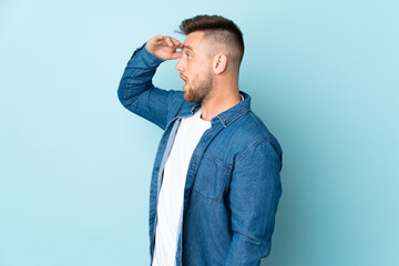 Russian handsome man isolated on blue background with surprise expression while looking side