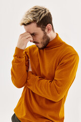 handsome blond man in orange sweater touches his head with his hand