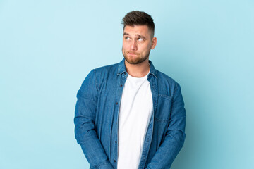 Russian handsome man isolated on blue background having doubts while looking up