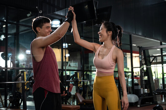 Cheerful young man and woman giving high five after a successful workout session in a modern fitness club 