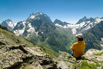 Naklejka premium A girl on the edge of a cliff admires the mountain peaks