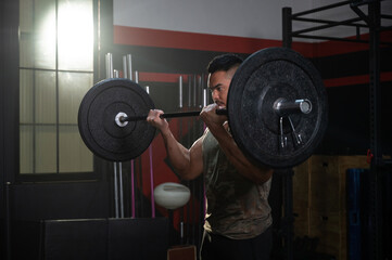 A young handsome Asian man exercises using a barbell equipment, in a modern sports club on a dark background concept.