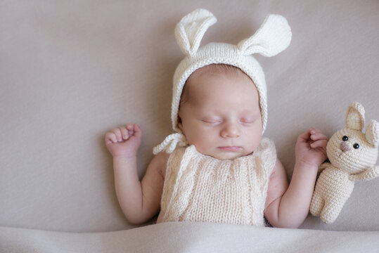 Baby in a knitted rabbit hat with ears and a bunny toy in a beige light blanket. Spring photo. Easter and children. Happy motherhood. Happy easter 