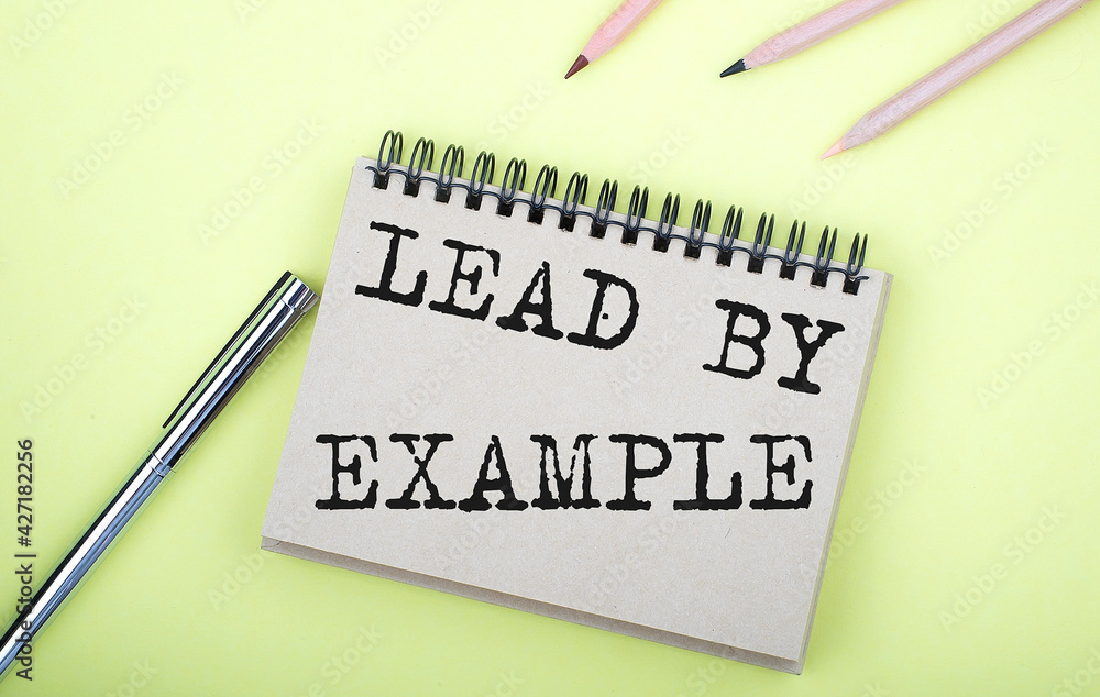 Poster lead by example text on the notebook with pen on the yellow background