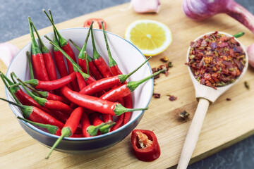 red chilli pods in bowl with spices and ingredients lie on wooden chopping board, close-up