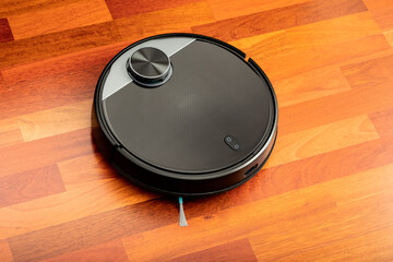 Black automatic vacuum cleaner robot in a house to clean the floor and help in housework. Smart...