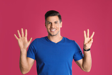 Naklejka premium Man showing number eight with his hands on pink background