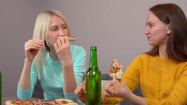 Relax with your friend. Two best happy girlfriends at home in the kitchen eating pizza and drinking beer. They laugh and smile. celebrating.