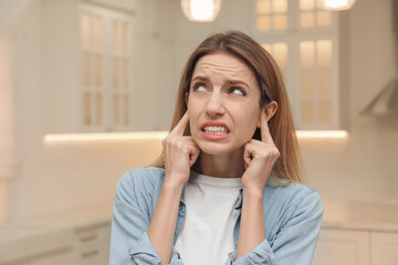 Fototapeta premium Emotional young woman covering her ears with fingers at home