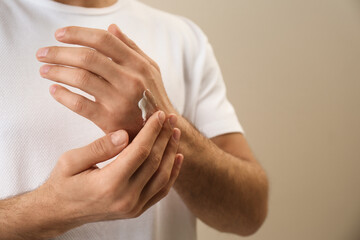 Man applying cream onto hand on beige background, closeup