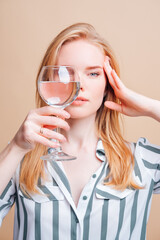 Beautiful red-haired girl looking through a glass with clear water on a light background.