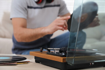 Man with vinyl record near turntable indoors, closeup