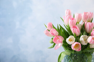 Beautiful bouquet of tulips in glass vase against light background. Space for text