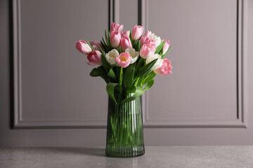 Beautiful bouquet of tulips in glass vase on grey table