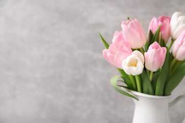 Beautiful bouquet of tulips in jug against grey background. Space for text