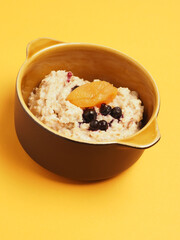 Delicious organic porridge with blueberries and apricot on a yellow table