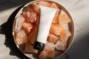 Unbranded tube with body care cosmetics lies on crystals of pink himalayan salt. Spa and wellnes concept - obrazy, fototapety, plakaty