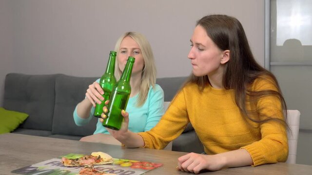 Relax with your friend. Two best happy girlfriends at home in the kitchen eating pizza and drinking beer. They laugh and smile. celebrating.