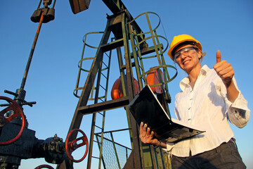 Successful female engineer with a notebook control the operation of the oil pump, low angle and close up of smiling young woman with safety goggles giving thumb up, job well done