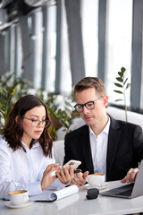Obraz premium Young business man female manager sit talking behind table in restaurant, use smartphone and laptop
