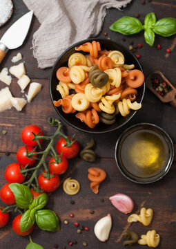 Fresh raw tricolore trottole pasta in black bowl with cherry tomatoes and basil, garlic and oil with parmesan cheese on wooden background.